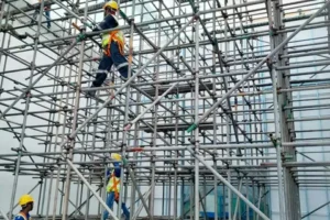 Construction workers wearing safety helmets and harnesses working on multi-level metal scaffolding.